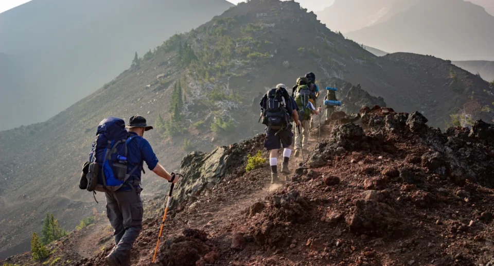 A group of hikers with backpacks climbing a rugged mountain trail surrounded by rocky terrain and distant peaks.